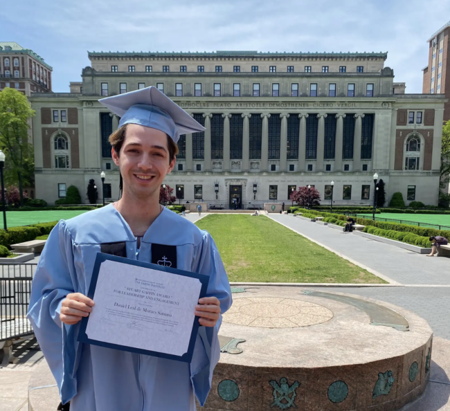 Male student in cap and gown in front of Columbia University