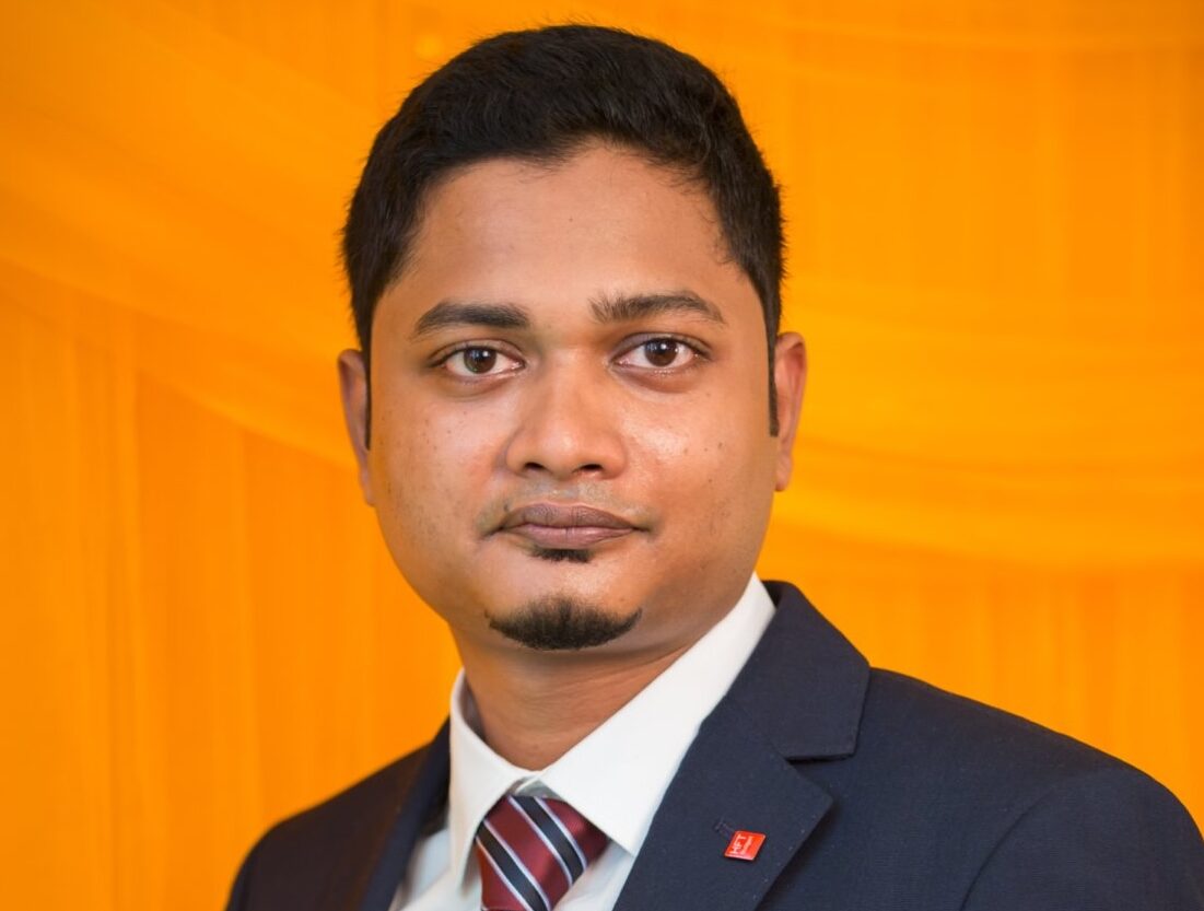 Headshot of a man in suit and tie in front of orange backdroup