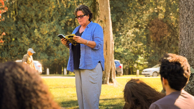 Woman reads to a group of students outdoors