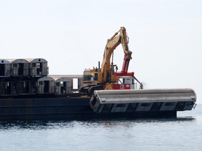 A subway car being pushed by a crane from a barge into the ocean.