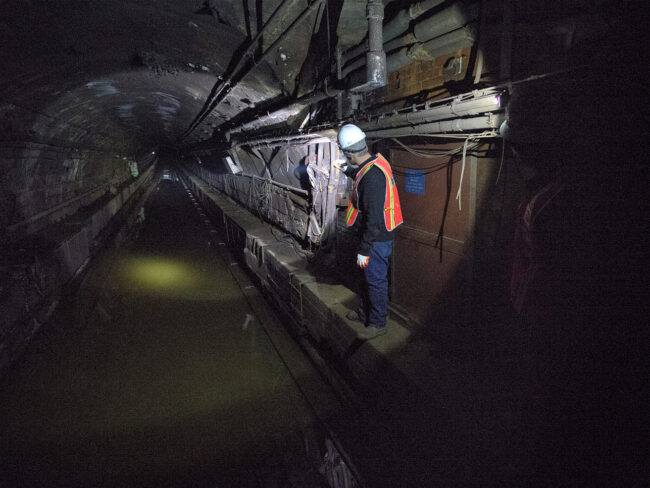 A subway worker shines a flashlight down a darkened, flooded tunnel.