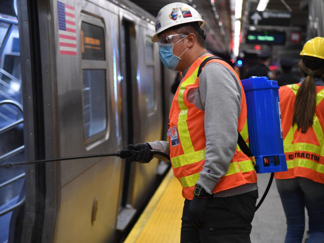 A masked MTA worker with a sprayer to sanitize subway cars.