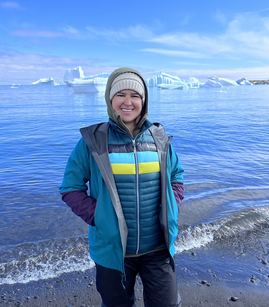 Person in winter gear stands in front of water and ice