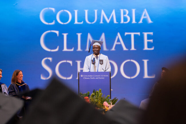 Student in cap and gown speaks at podium