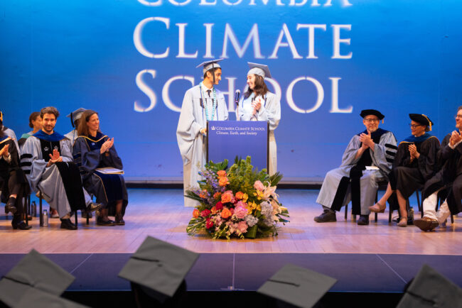 Two graduates stand on stage