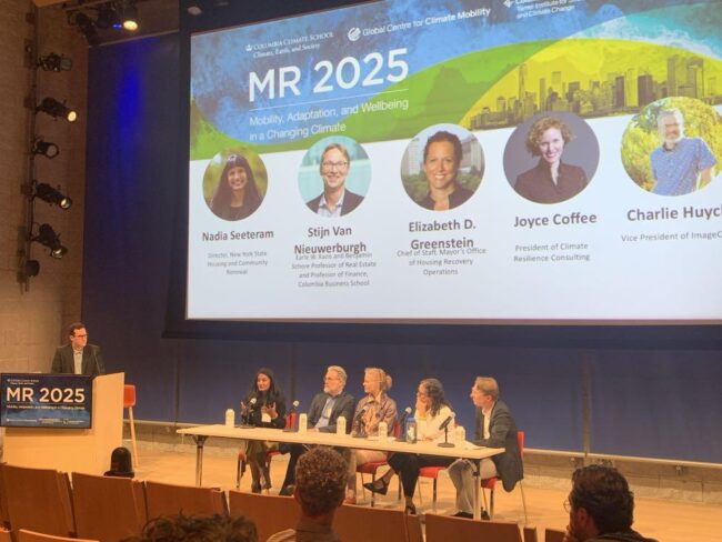 Panelists and speaker on a stage with a PowerPoint