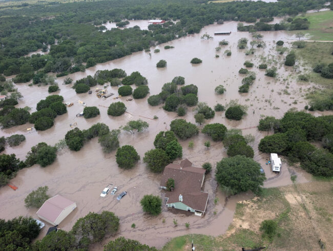The muddy Guadalupe River, with trees and houses under water,  near Kerrville, Texas, on July 5, 2025
